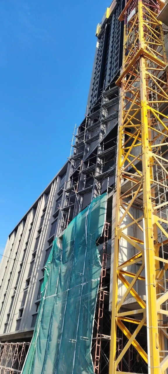 Netted facade scaffold beside a crane